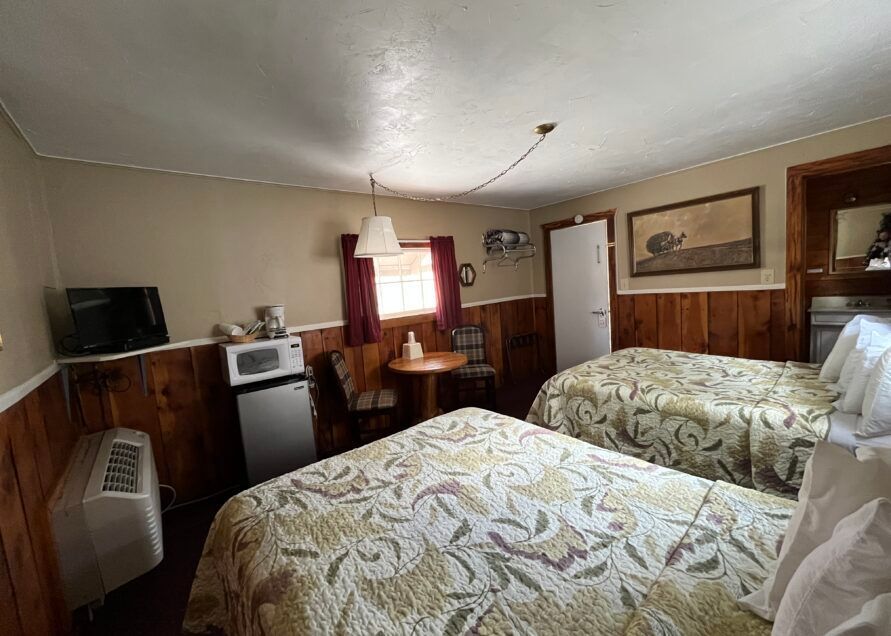 A small motel room with two beds, wood paneling, and a small table.
