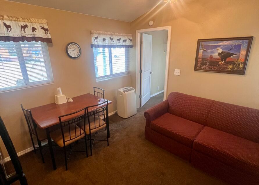 A small, furnished room with a table and chairs, a sofa, and a doorway. 
