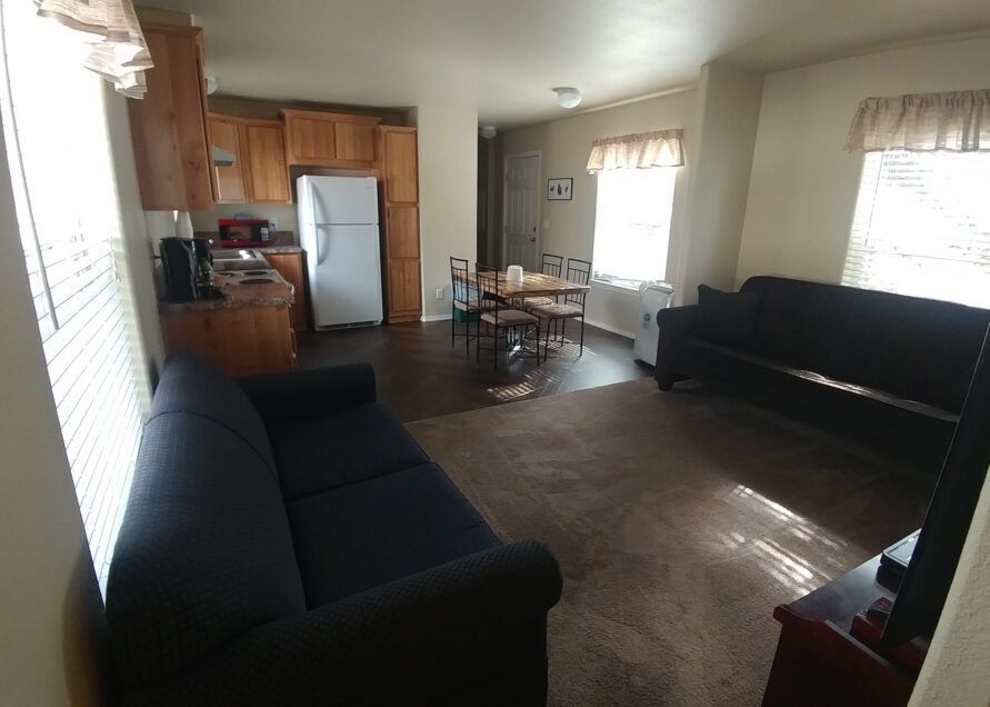 A living room with two dark blue couches, a dining table, and a kitchen.