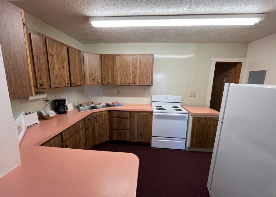 Kitchen with wooden cabinets, pink countertops, white appliances, and a red floor. A refrigerator is in the foreground.