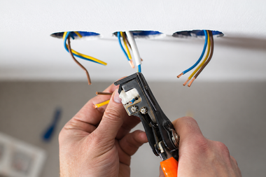 Hands stripping wires from a ceiling electrical box with a wire stripper tool