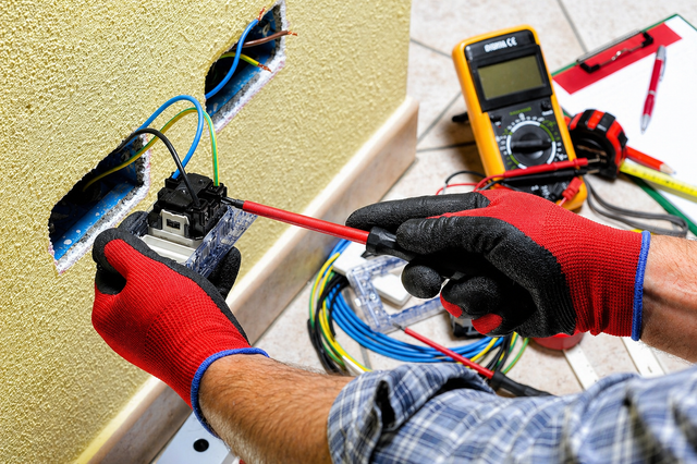Gloved hands repairing electrical wiring with a multimeter and tools on a workbench
