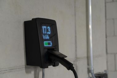 Wall-mounted black EV charger with a plugged-in cable and lit display panel