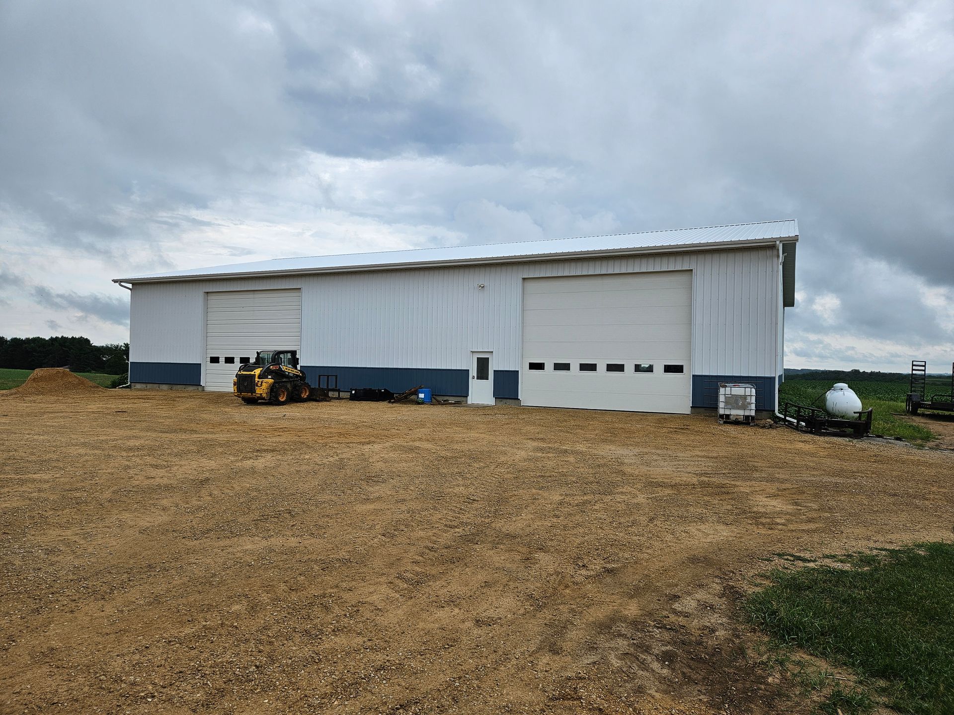 A large white building with a large garage door is sitting in the middle of a field.