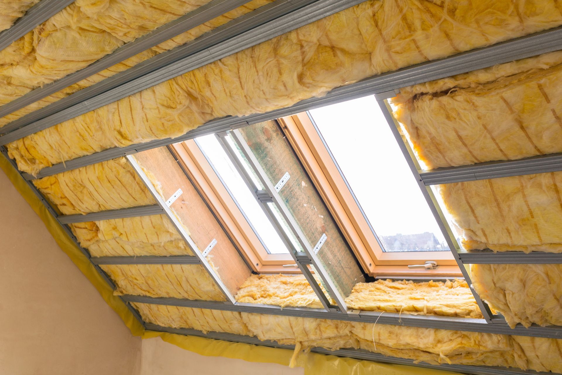 Attic space with yellow insulation around a skylight; metal framing visible.