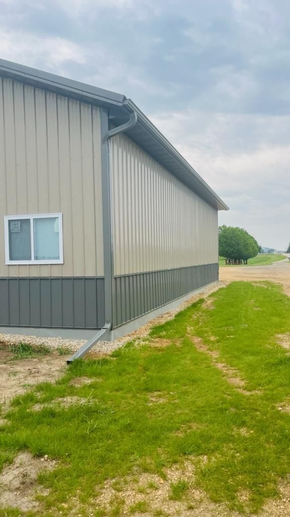 A large metal building with a lot of windows is sitting on top of a lush green field.