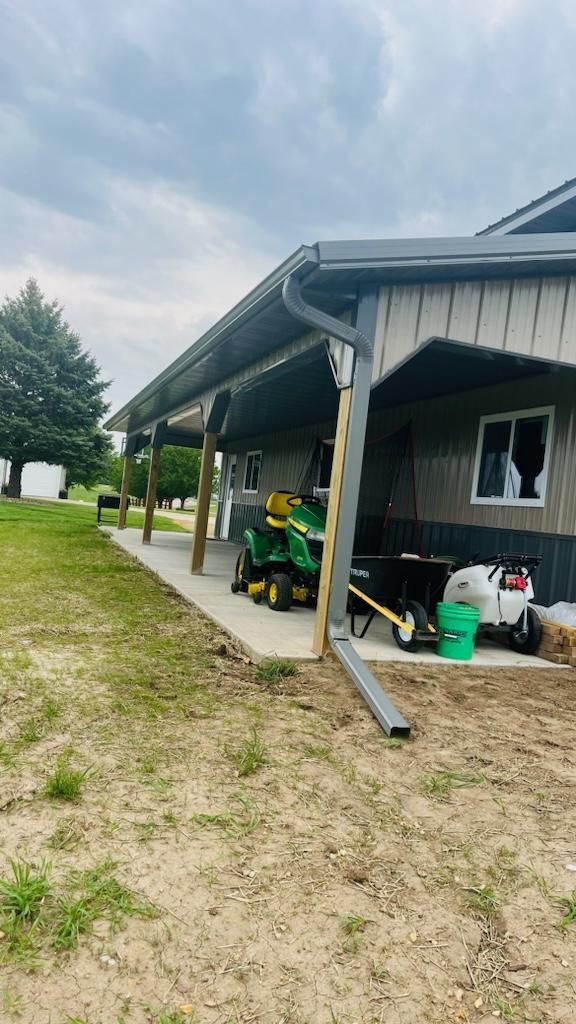 A john deere lawn mower is parked under a covered porch.