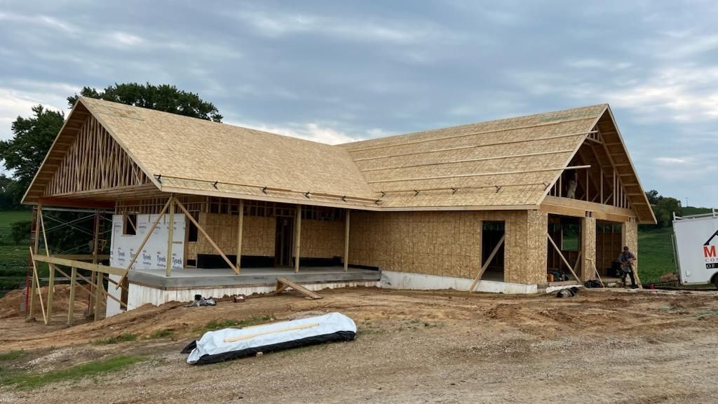 A large wooden house is being built in a dirt field.
