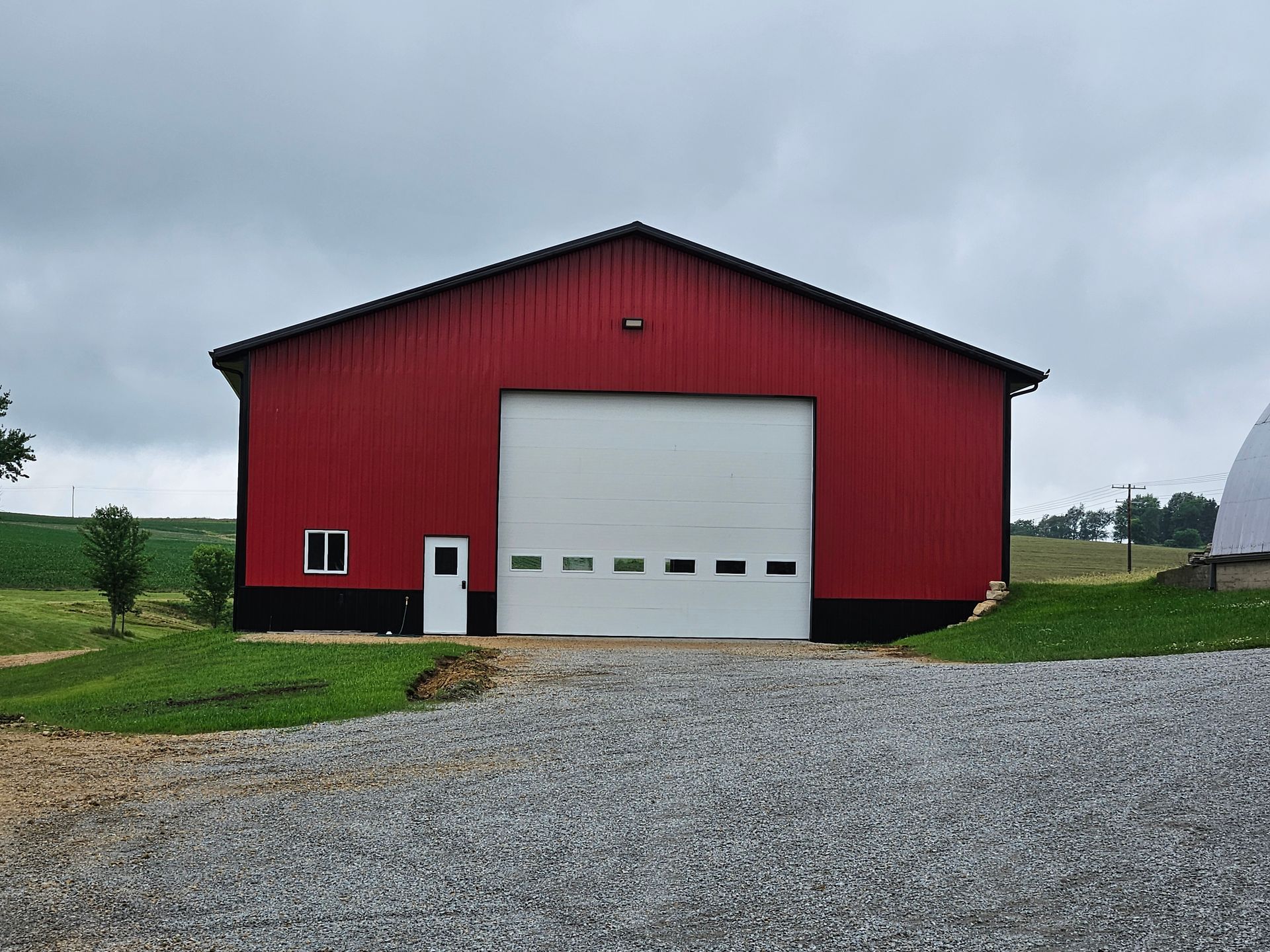 A red barn with a white garage door is sitting on top of a gravel road.