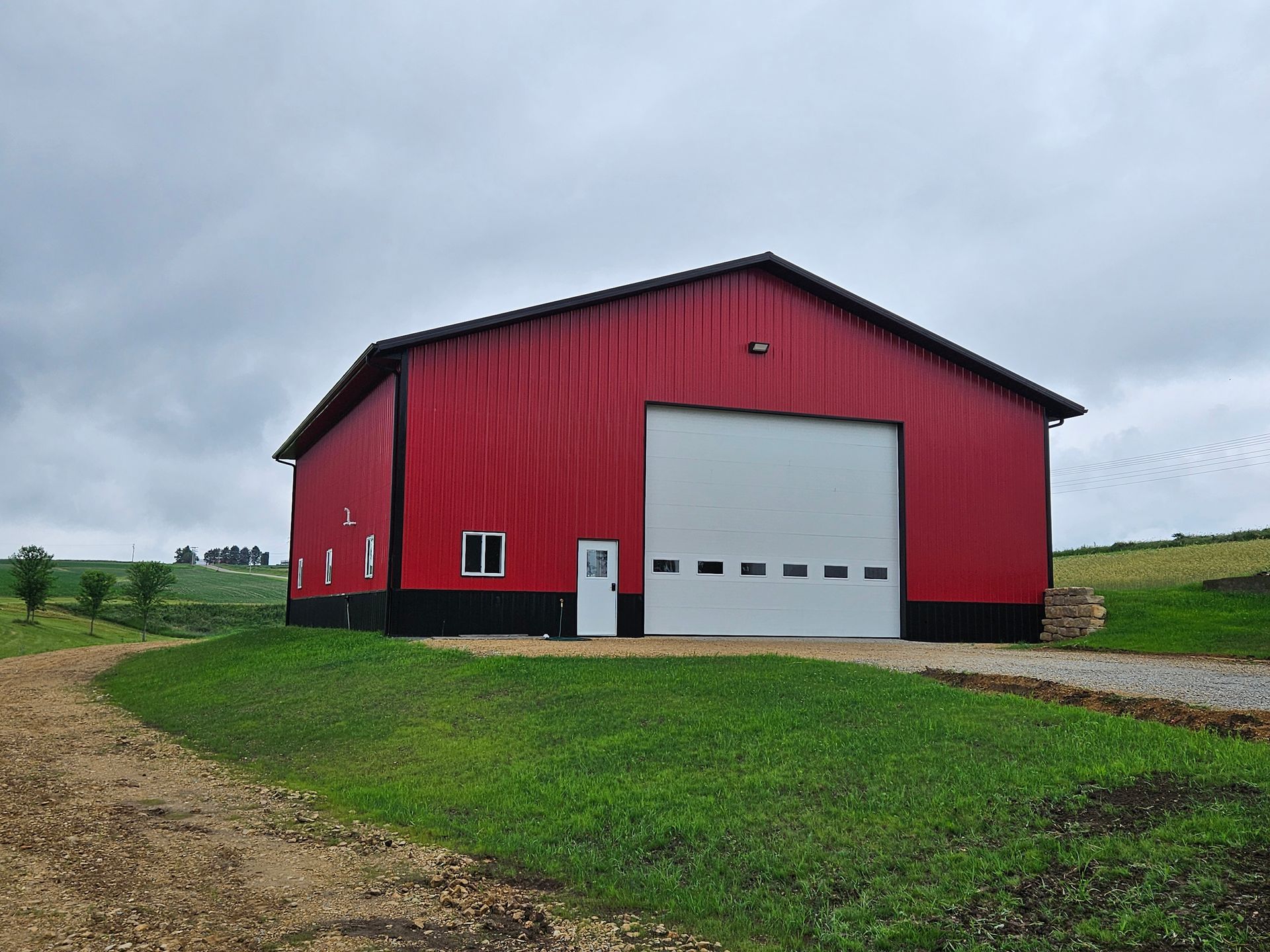 A red barn with a white garage door is sitting in the middle of a grassy field.