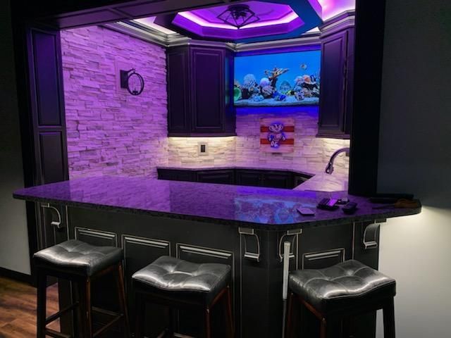 A kitchen with a bar and stools and a television on the wall.