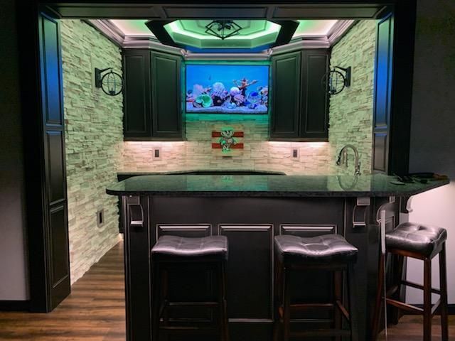 A kitchen with a bar and stools and a television on the wall.