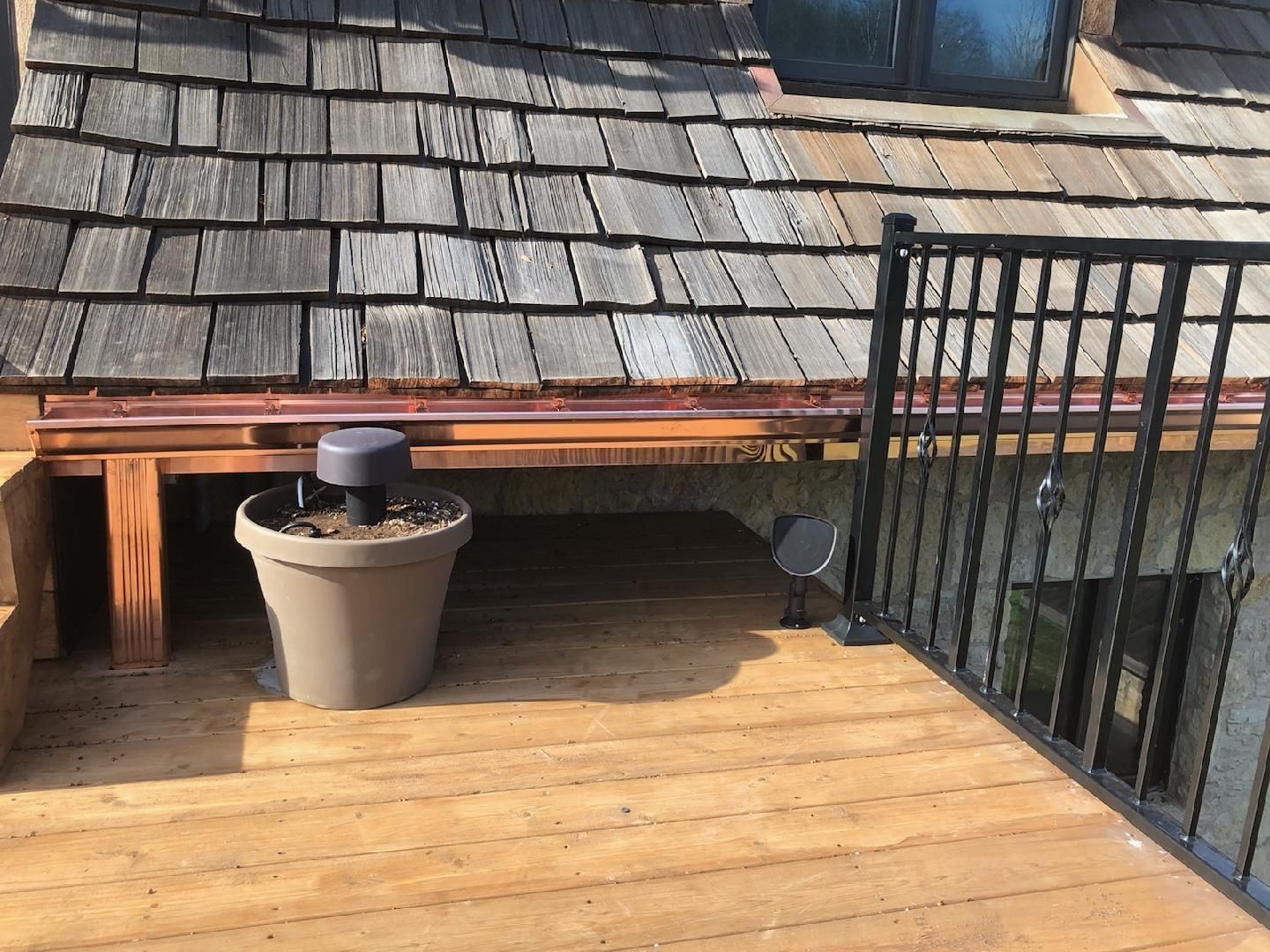 A potted plant is sitting on a wooden deck under a wooden roof.