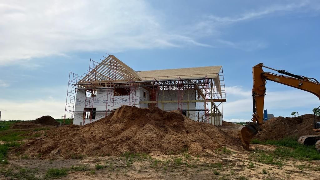 A large pile of dirt is in front of a house under construction.