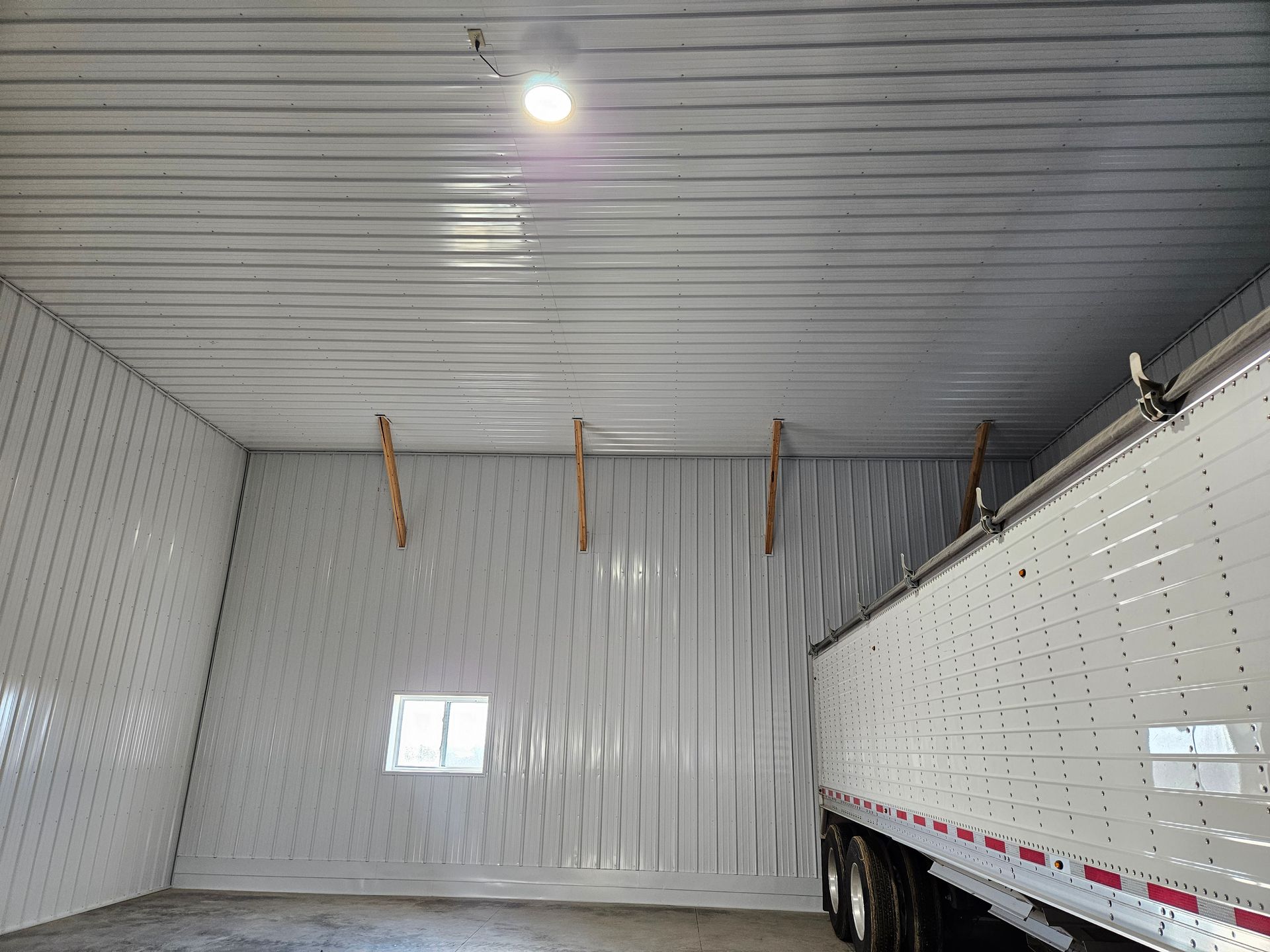 A trailer is parked in a garage with a light on the ceiling.