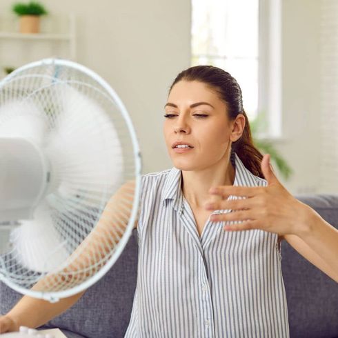 A woman is sitting on a couch in front of a fan.