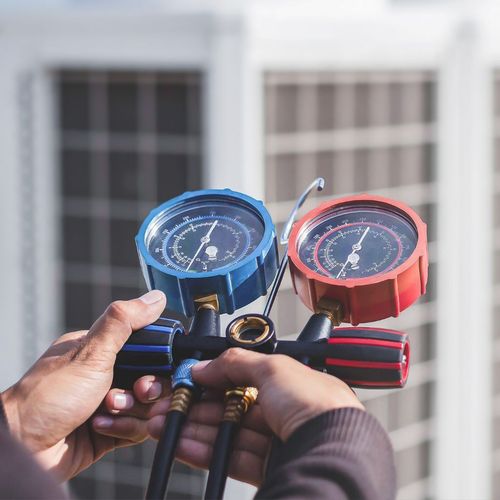 A person is working on an air conditioner with a gauge.