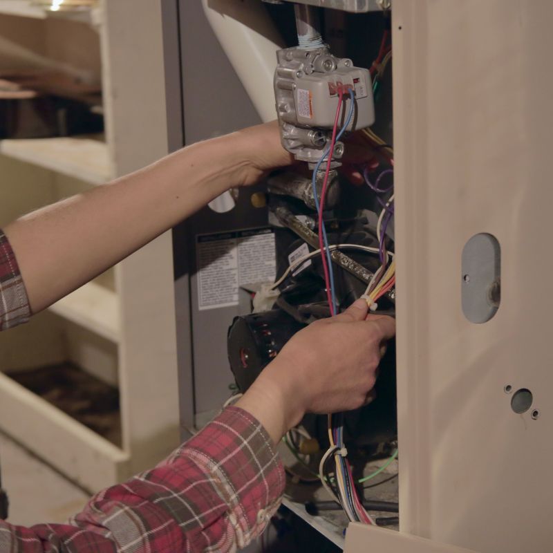A man in a plaid shirt is working on a heater