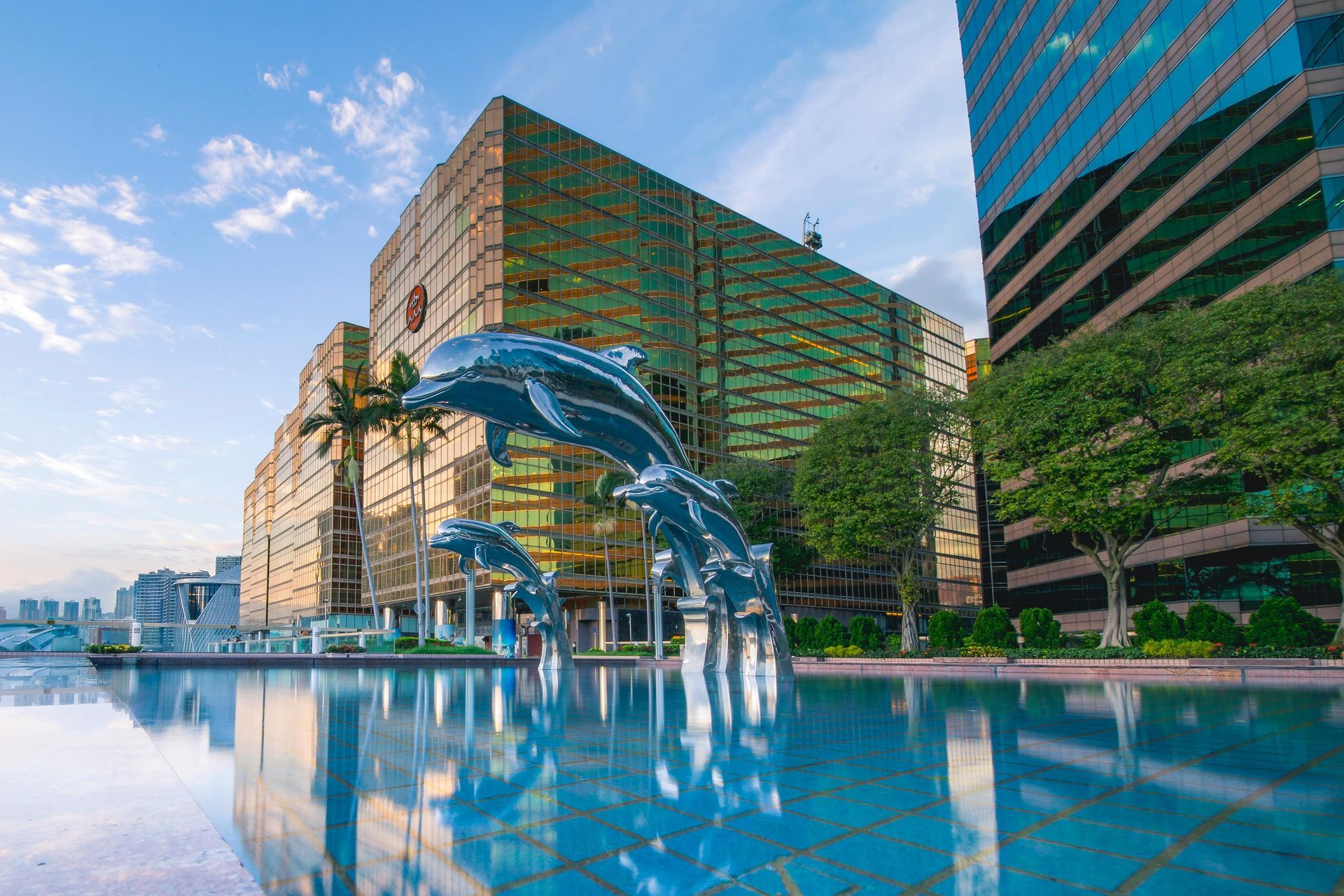 Large golden building with dolphin sculptures in a reflecting pool. Blue sky.