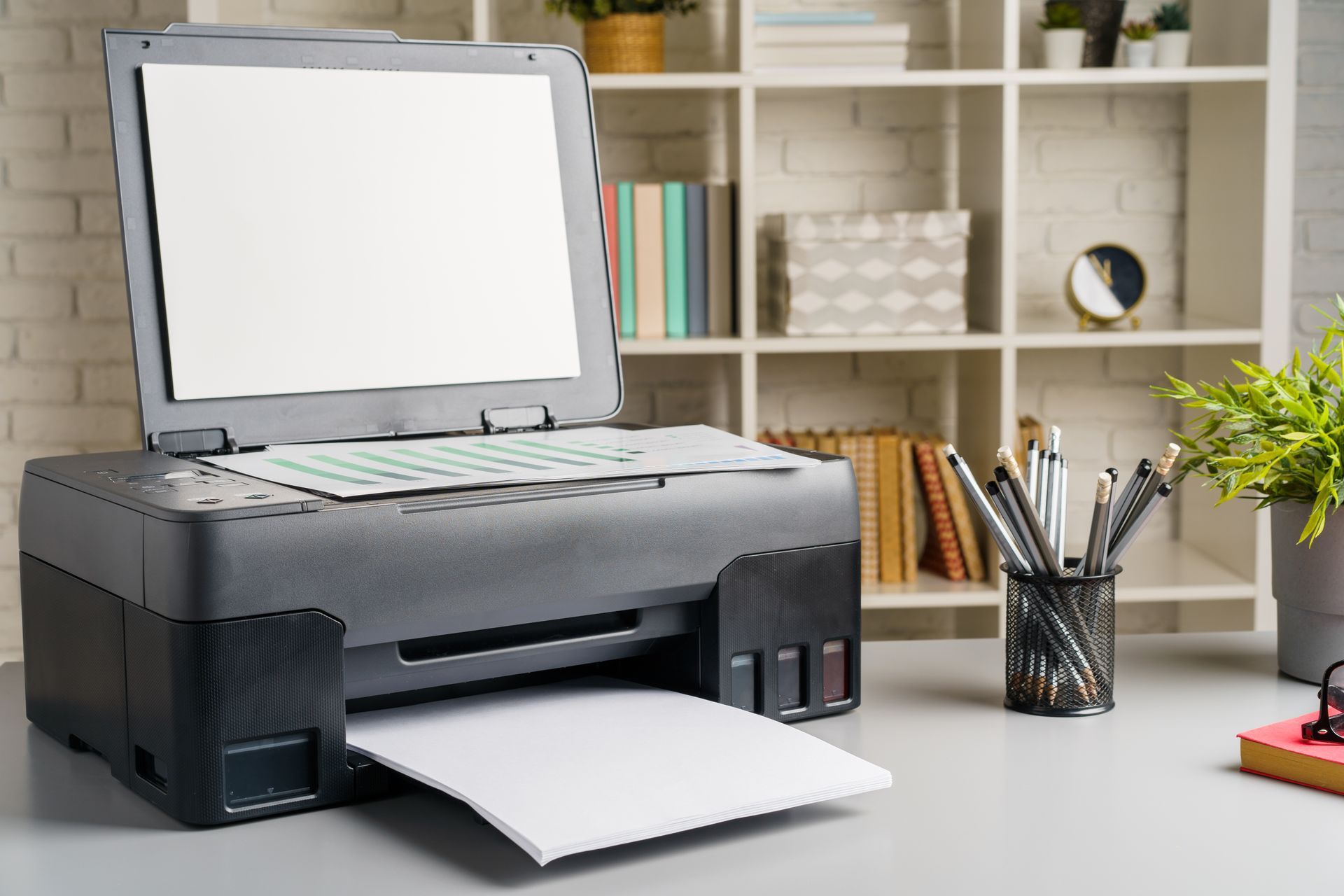 A printer is sitting on a desk next to a pen holder.