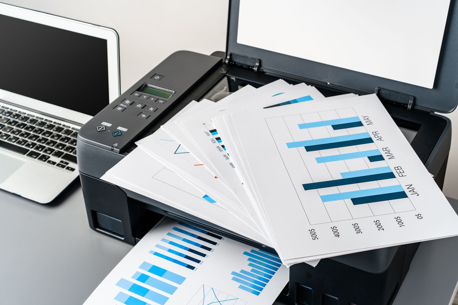 A printer is printing a bunch of papers next to a laptop