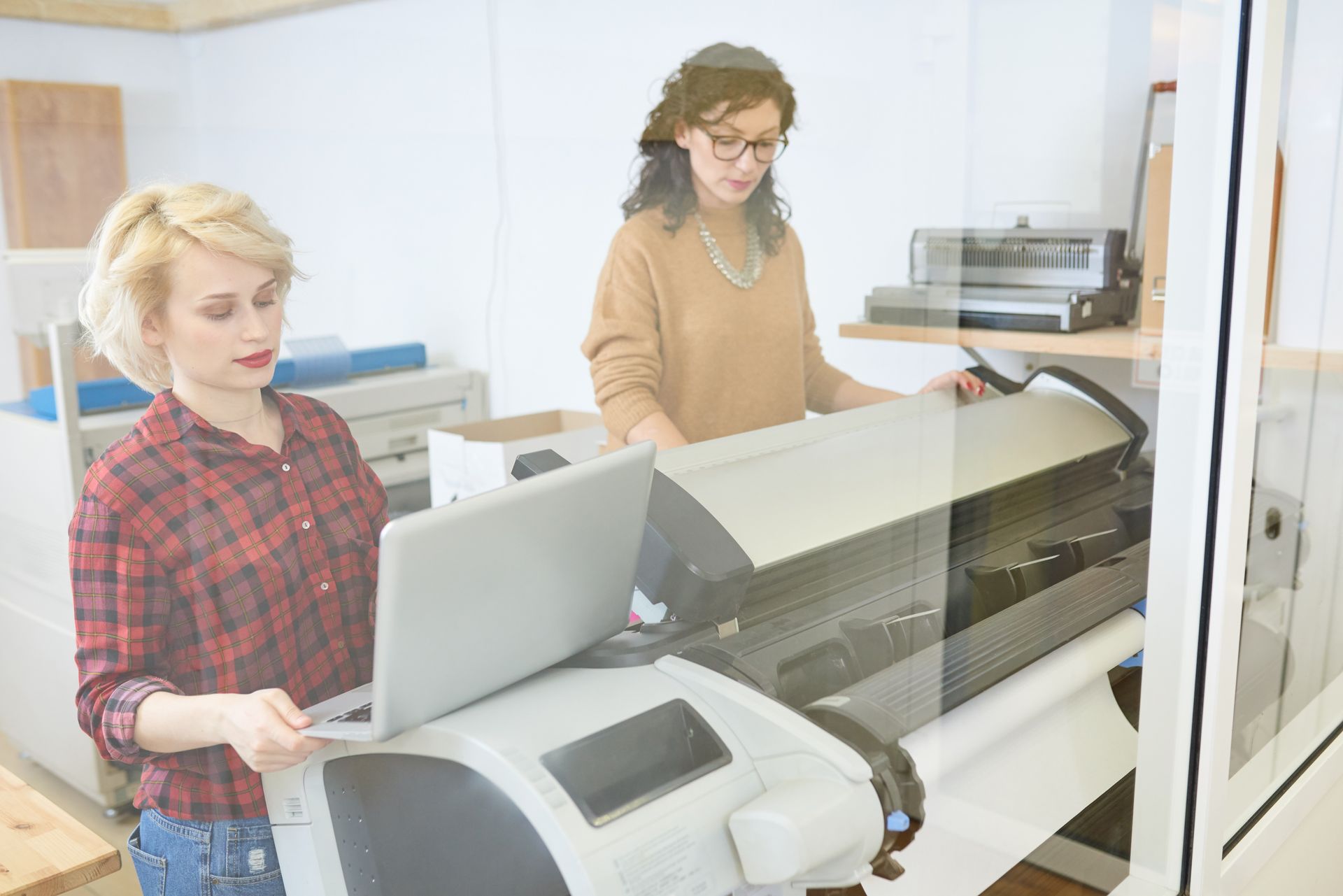 Two women are working on a printer in an office.