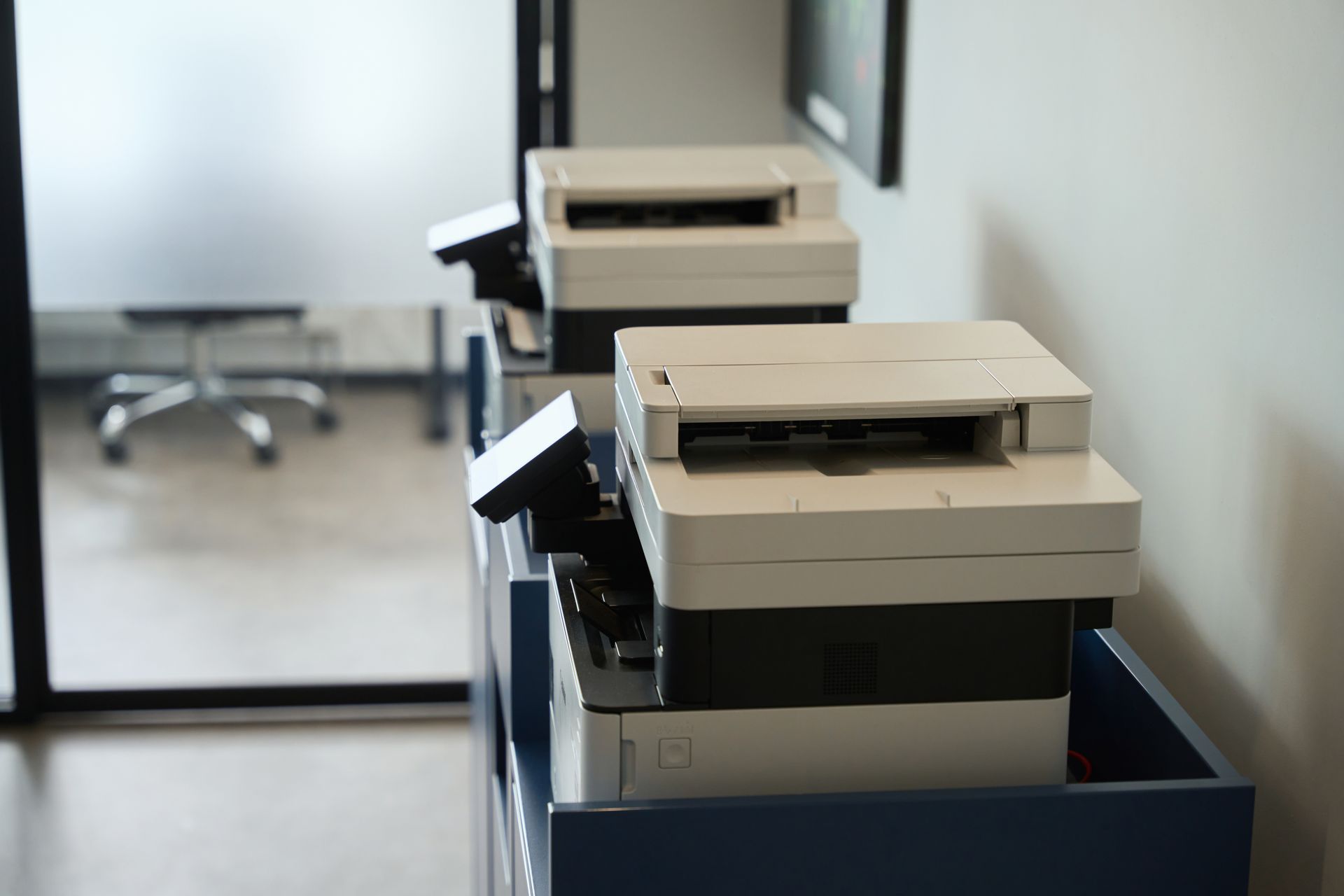 A man in overalls is standing in front of a printer and writing on a clipboard.