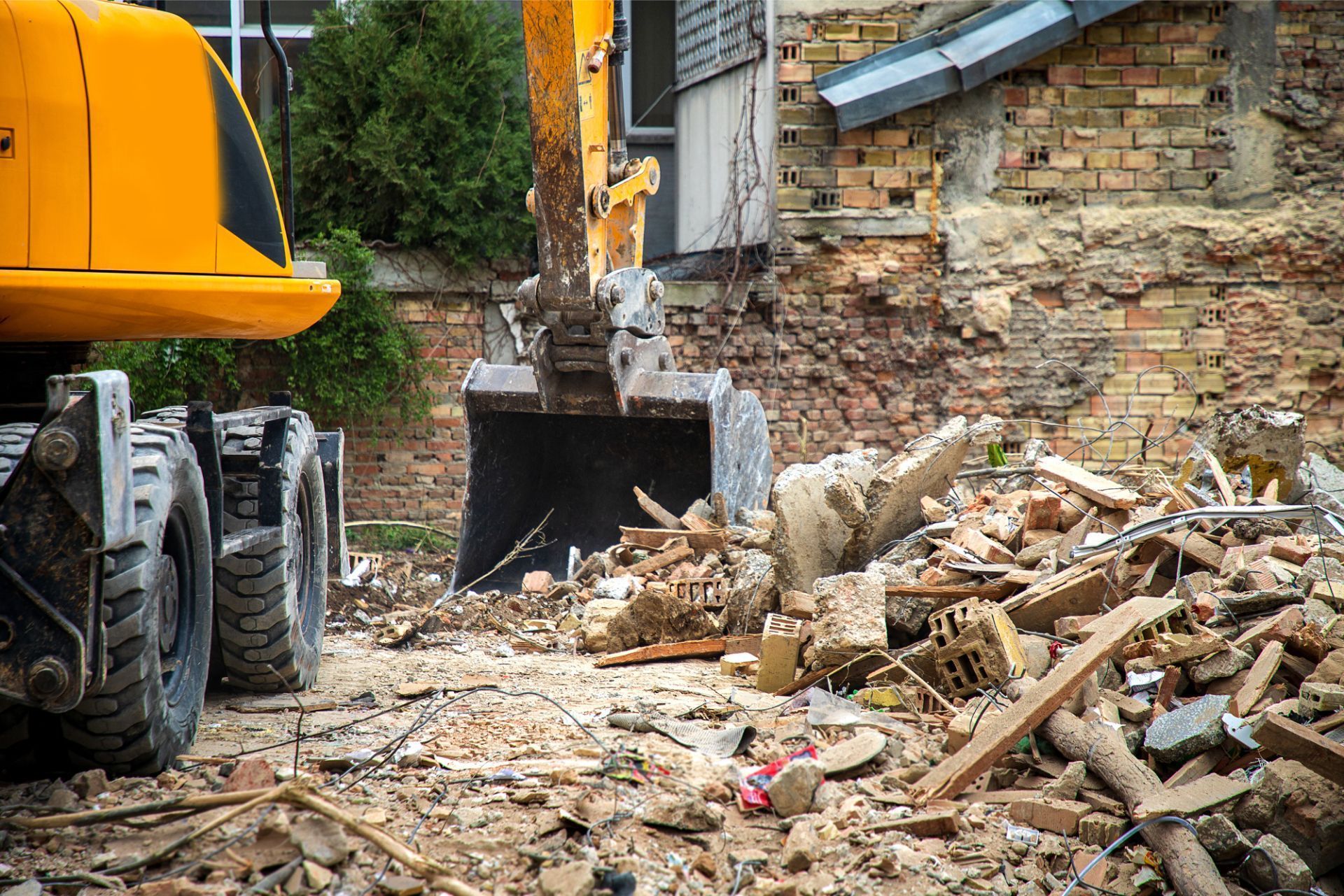 A yellow excavator is demolishing a brick building.