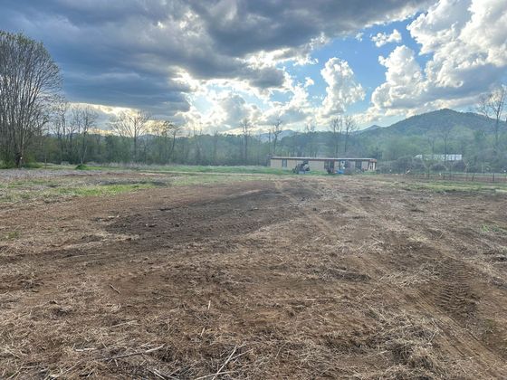 A dirt field with mountains in the background and a cloudy sky.