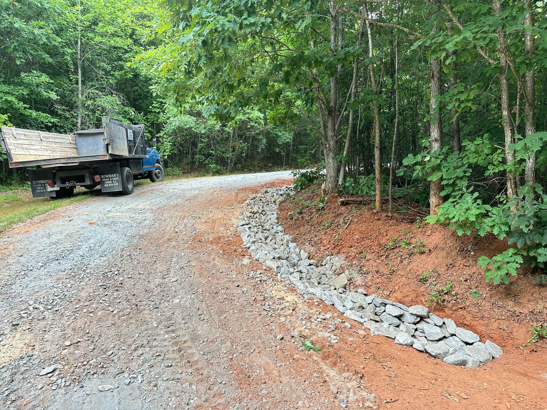 A dump truck is parked on the side of a gravel road.