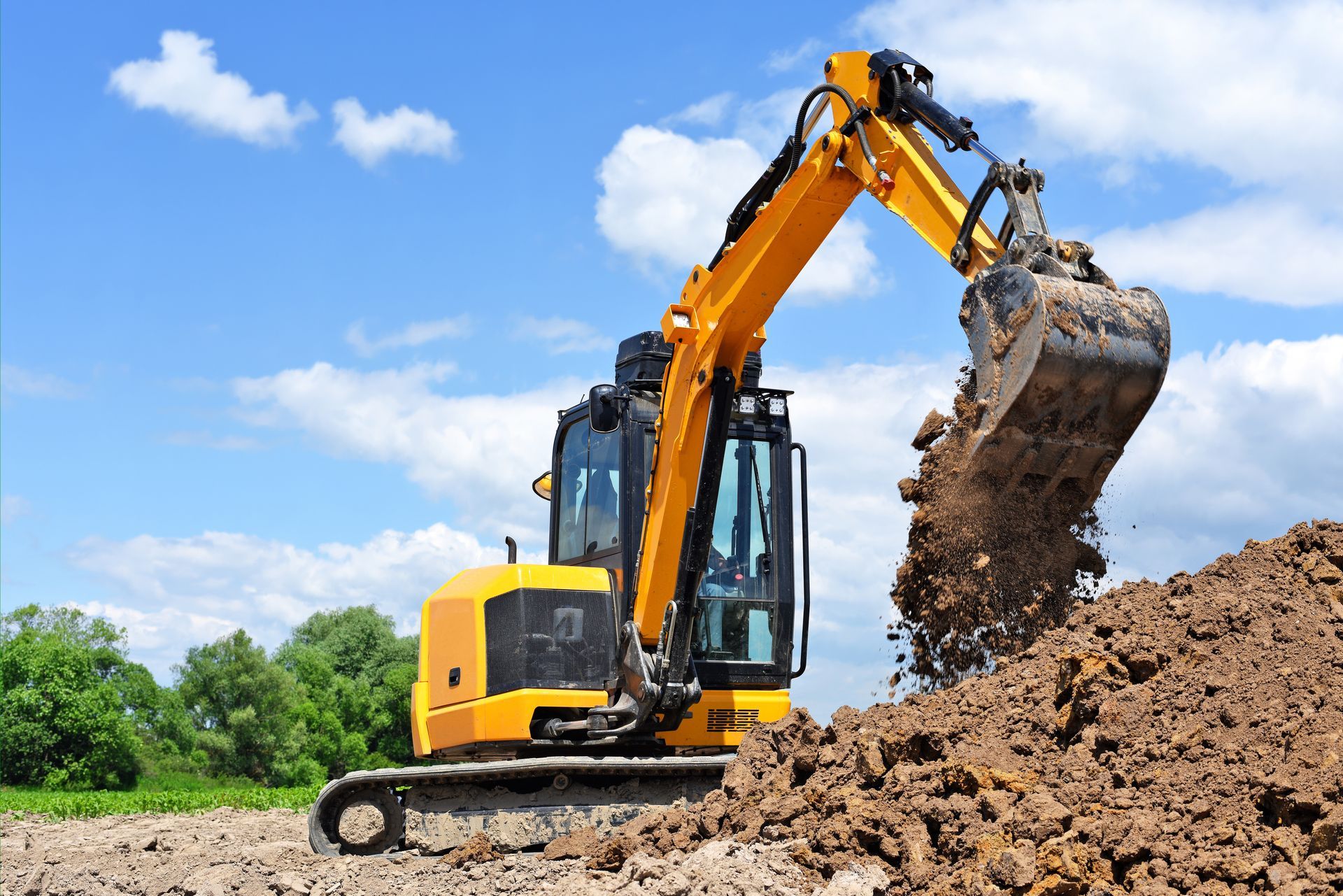 A yellow excavator is digging a pile of dirt in a field.