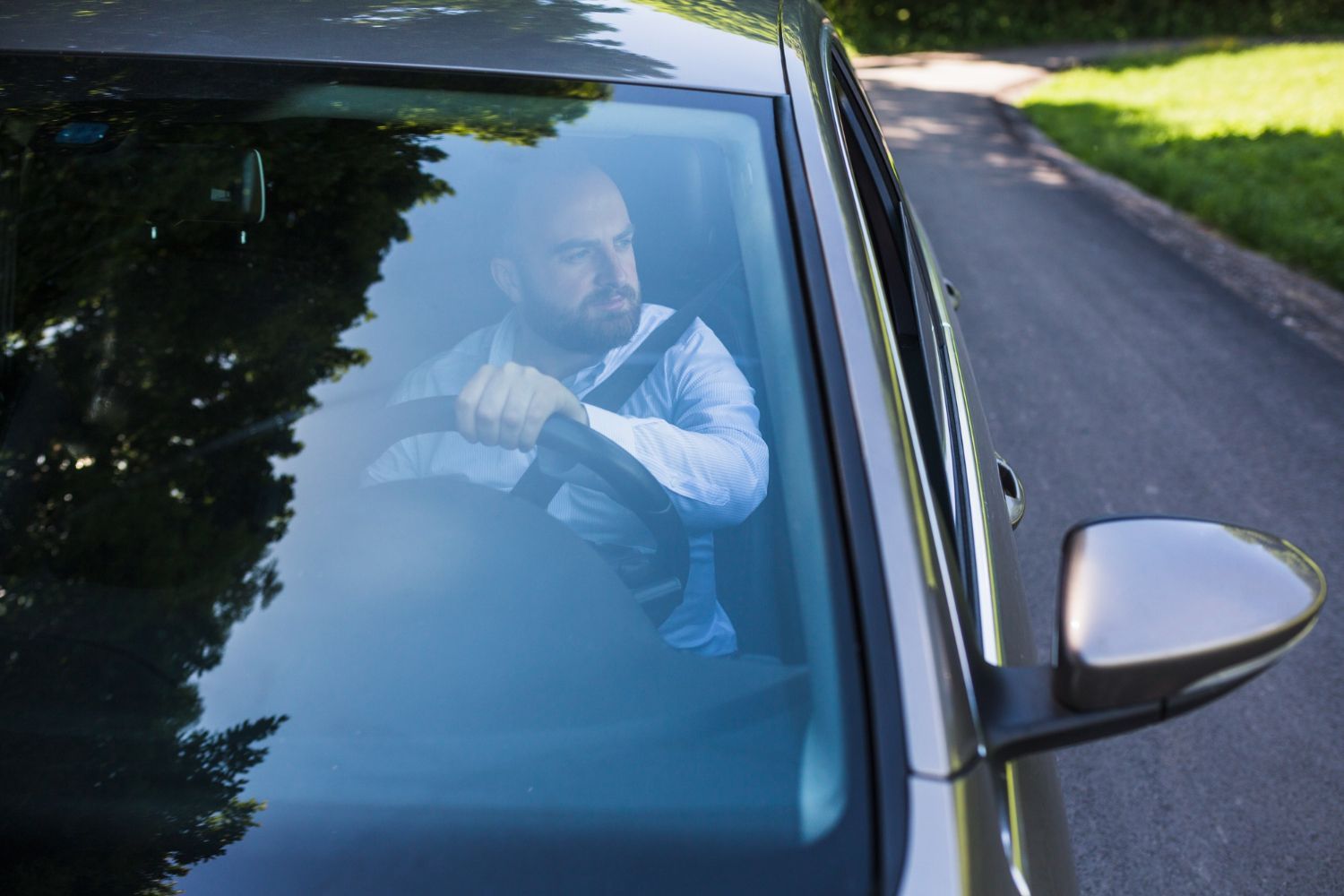 A man is driving a car down a road and looking out the window.