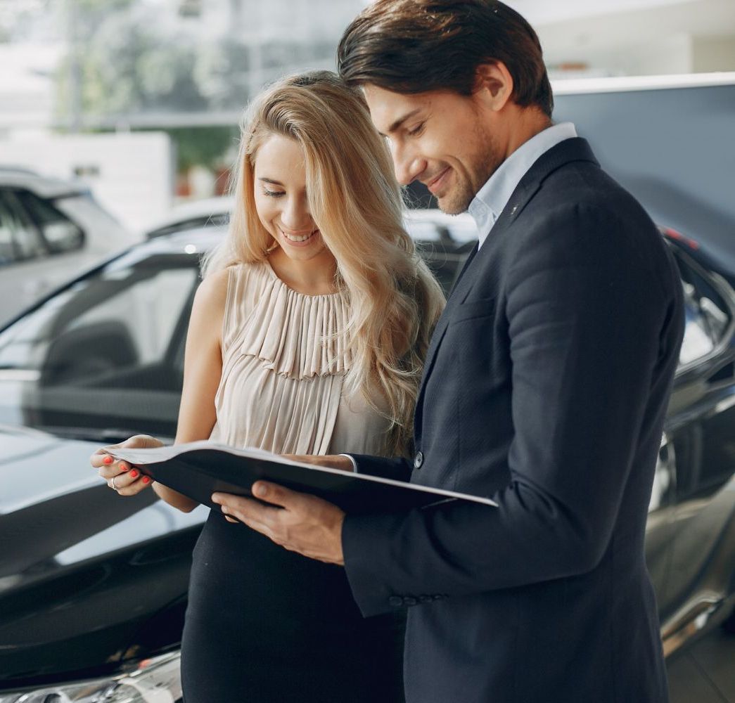 A man and a woman are looking at a book in front of a car.