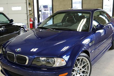 A blue bmw is parked in a garage next to a black car.