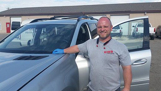A man is standing next to a silver car in a parking lot.