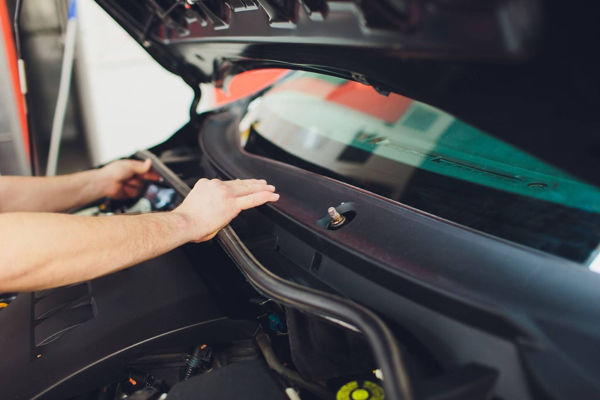 A man is working on the windshield of a car with the hood open.