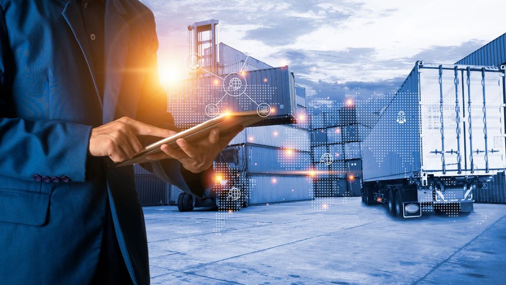 A man in a suit is using a tablet in front of a warehouse.