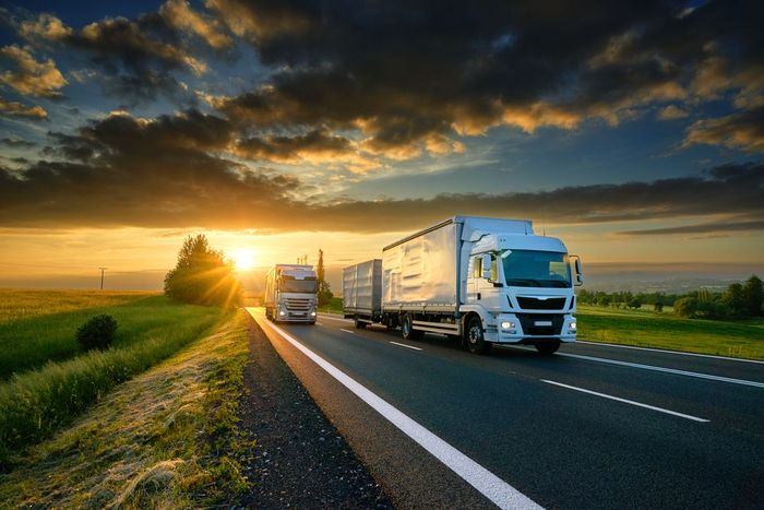 Two trucks are driving down a highway at sunset.