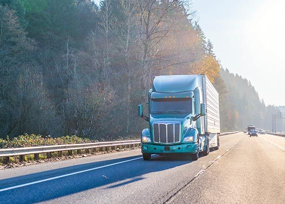 A semi truck is driving down a highway next to trees.