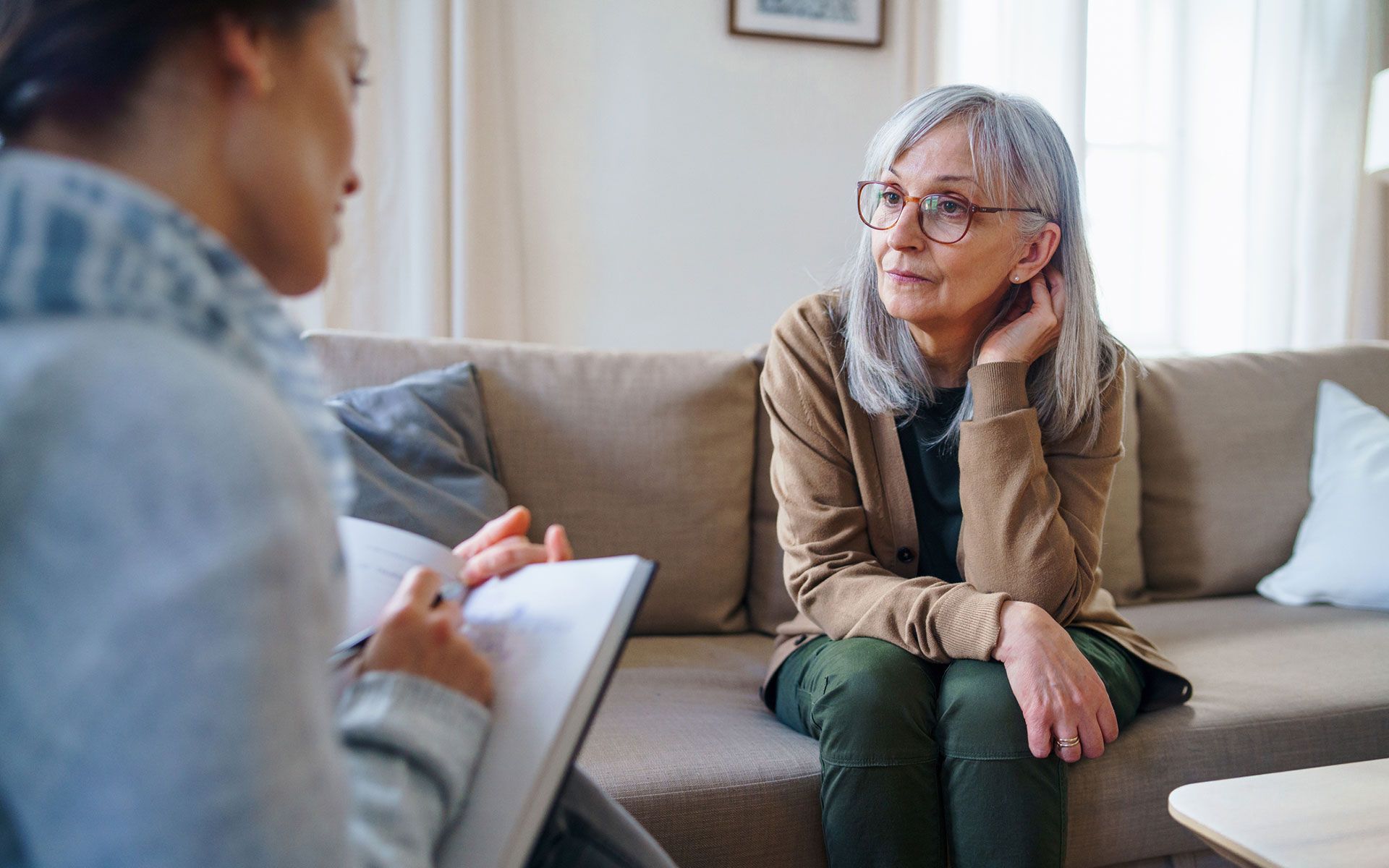 A woman is sitting on a couch talking to another woman.