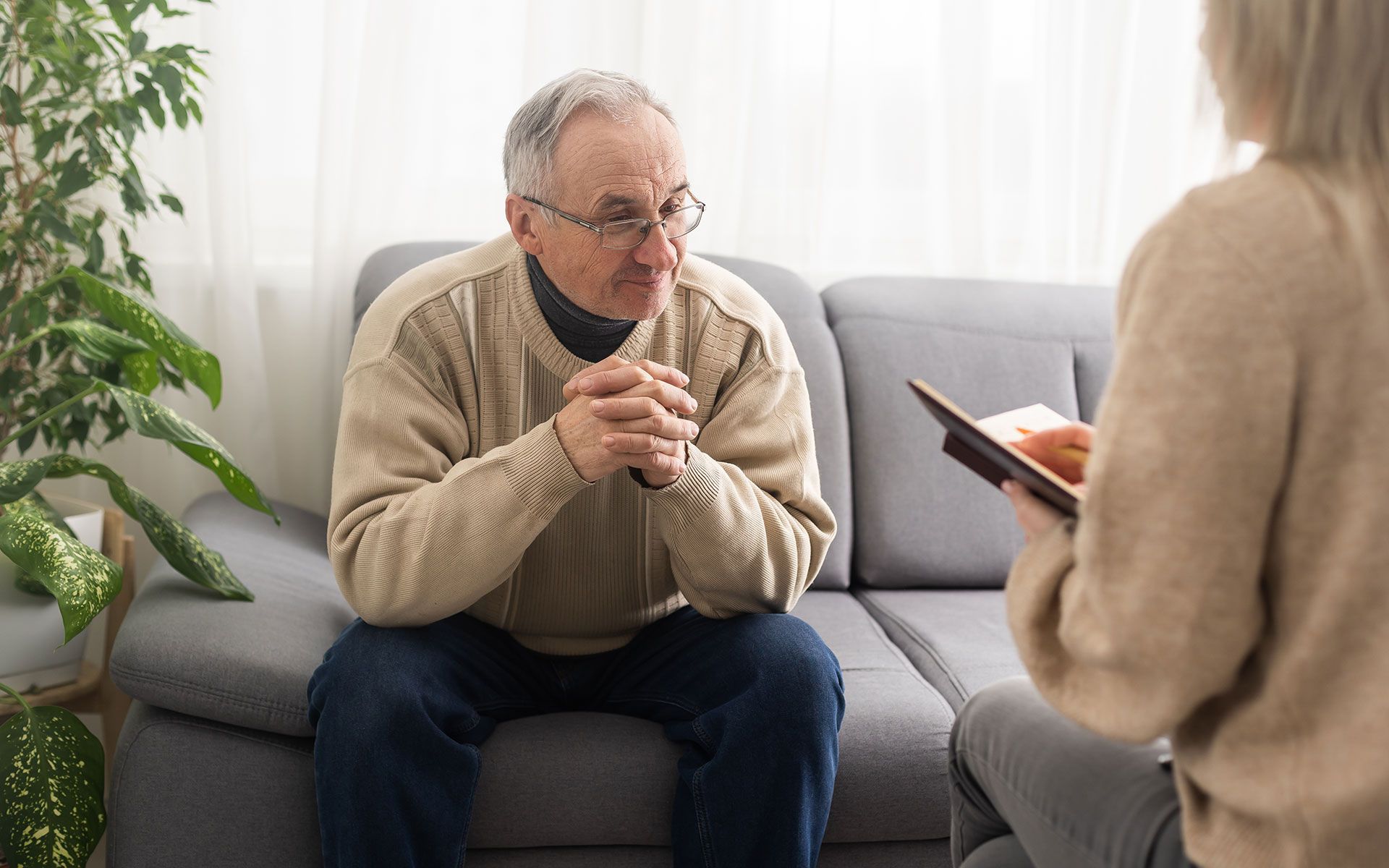 An elderly man is sitting on a couch talking to a woman.