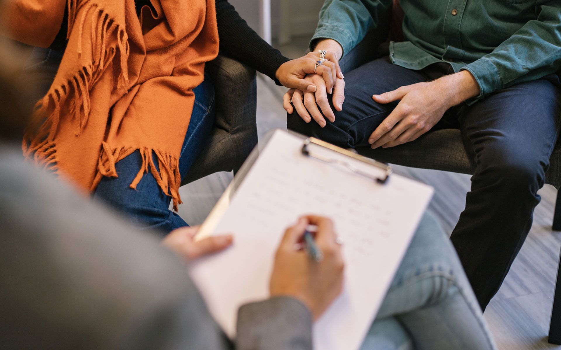 A man and a woman are sitting in a chair holding hands while a person writes on a clipboard.