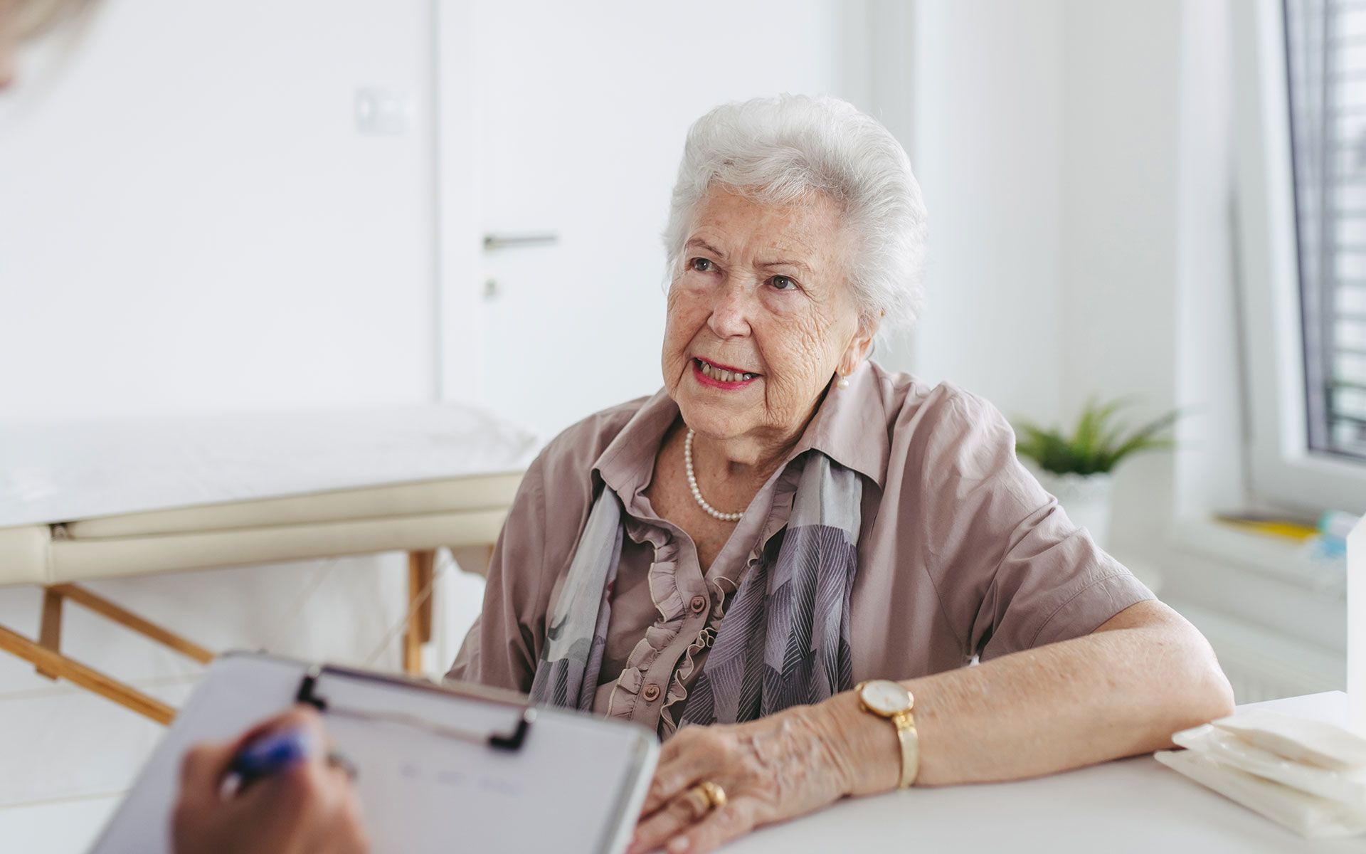 An elderly woman is sitting at a table talking to a doctor.