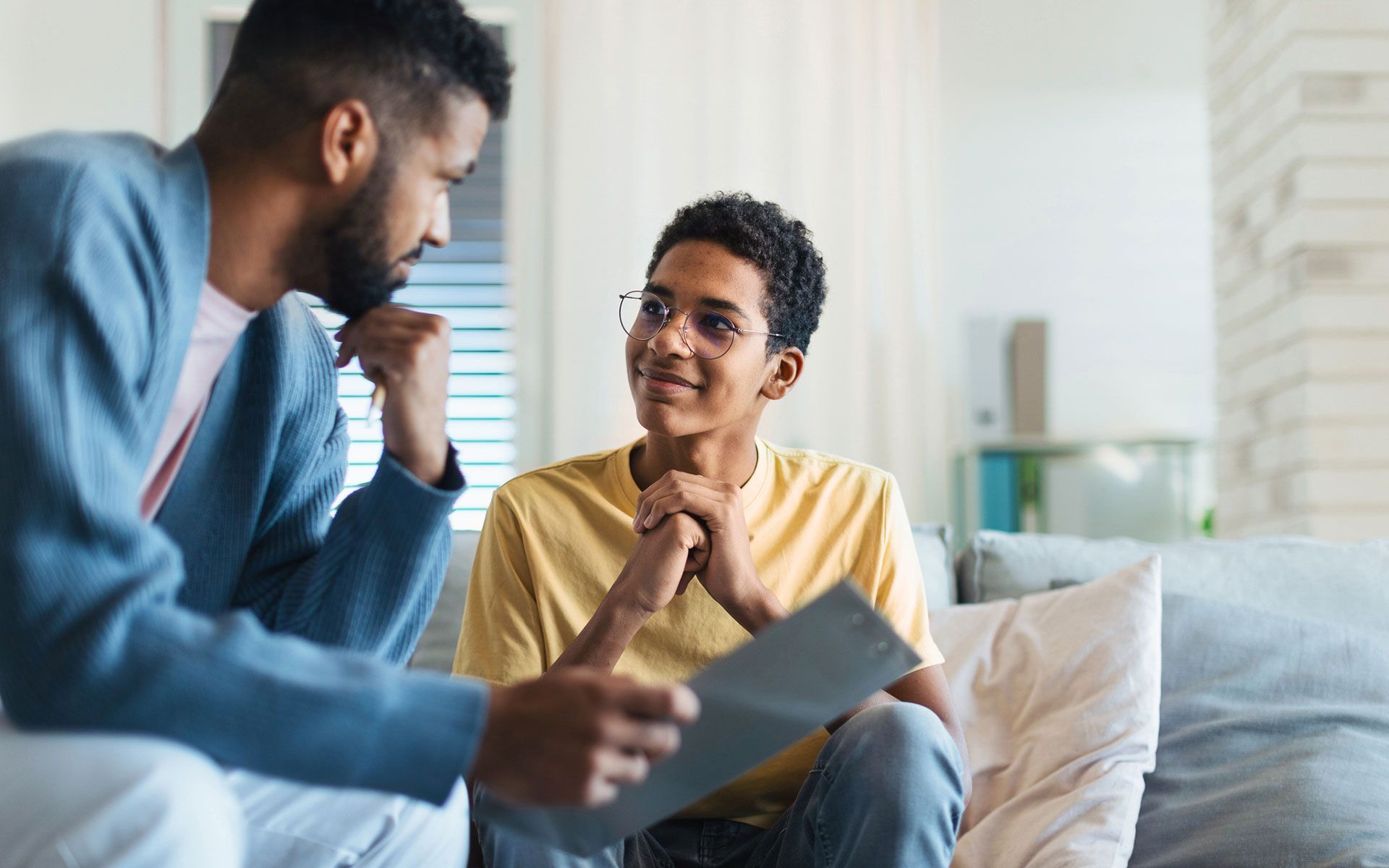 A man and a boy are sitting on a couch talking to each other.