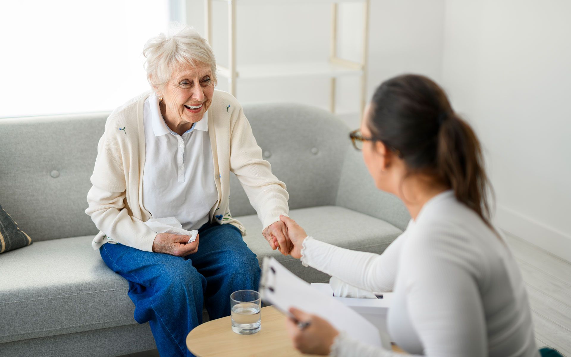An elderly woman is sitting on a couch talking to a nurse.