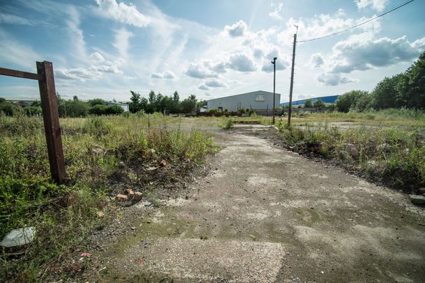 A dirt road going through a grassy field with a fence in the background.