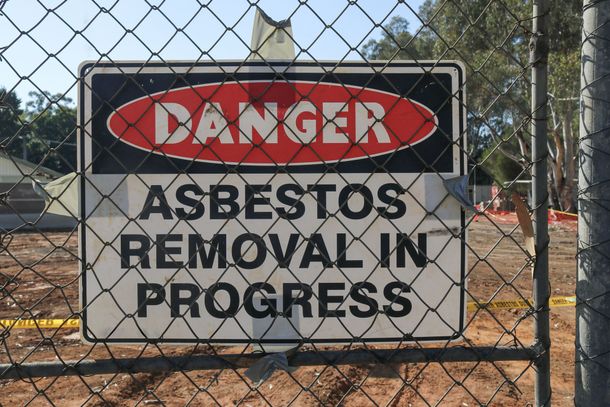 A sign on a chain link fence warns of asbestos removal in progress