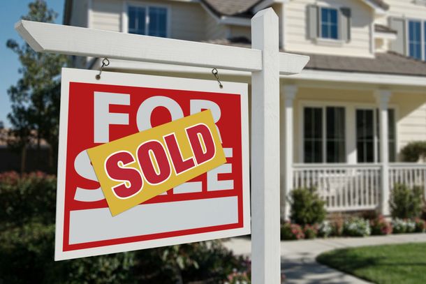 A for sale sign is hanging in front of a house