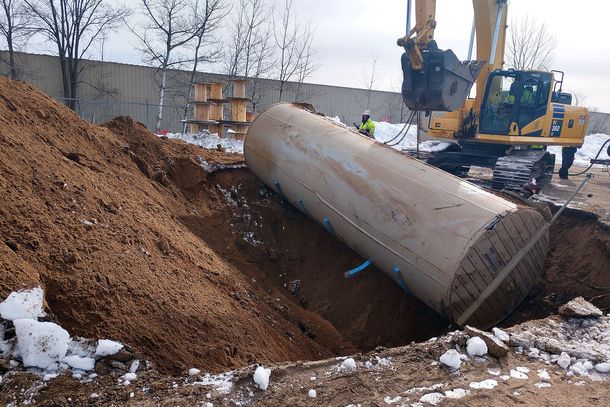 A large underground storage tank is being removed from the ground by a bulldozer.