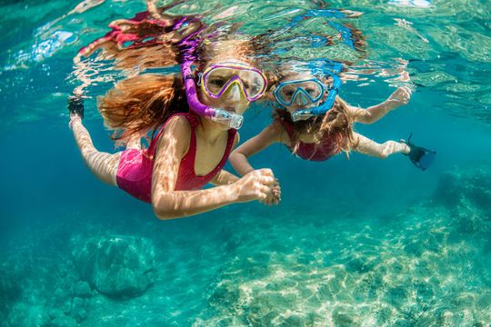 Two young girls are swimming underwater in the ocean.